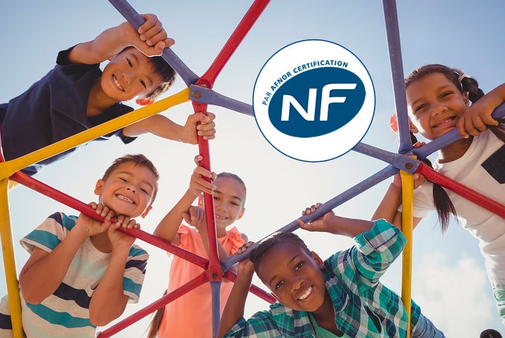Vue du dessous de cinq enfants qui jouent sur une structure en métal colorée. Sur l'image le logo NF nous donne une information de certification.