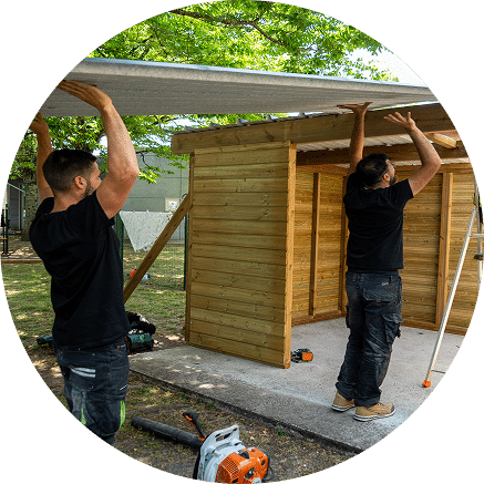 Deux techniciens construisent une cabane en bois. Ils portent le toit de la cabane.