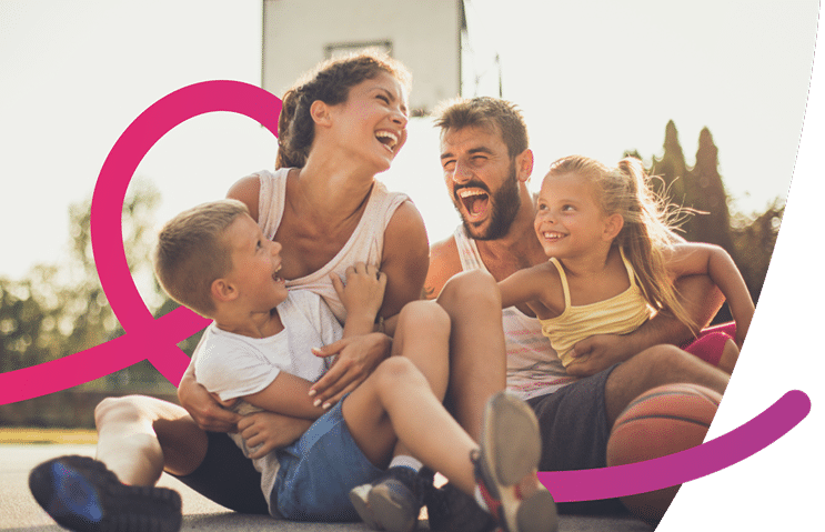 Une famille avec une femme, un homme et deux enfants rient. Ils sont assis sur un espace de jeu extérieur.