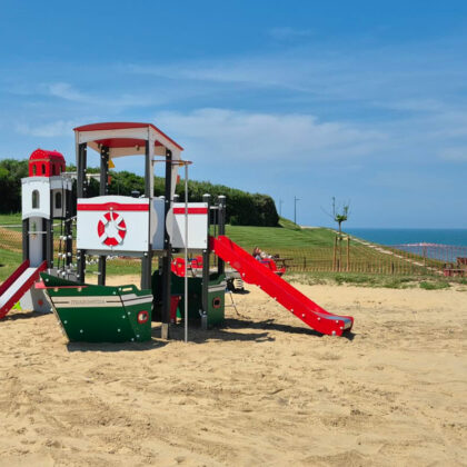 Aire de jeux sur sable proche de la mer. Thème bateau, bouée, vert, rouge et blanc. Toboggan et structure robustes